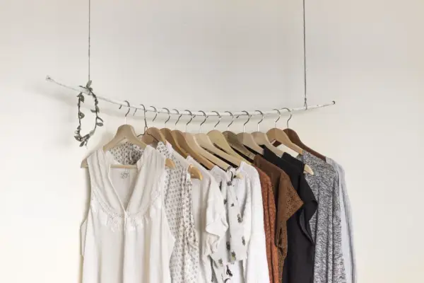 Eine minimalistische **Kapsel Garderobe** mit hellen, gemusterten und erdigen Kleidungsstücken, die an einem Ast hängen.